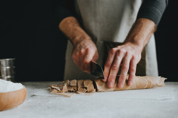 Unrecognizable man cutting the dough with a knife on a white background