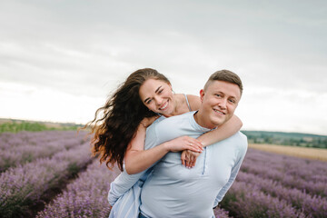 Piggyback. Couple hugging in violet lavender field of flowers. Man and woman standing, enjoys floral glade, summer nature. Loving family walking at sunset. France, Provence. Honeymoon trip, traveling.