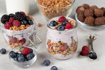 Chocolate granola with berries, chia seeds and natural yogurt in two jars on gray background