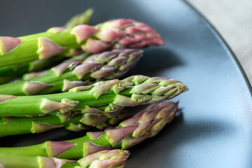 Fresh green asparagus on black plate. Healthy vegan raw food concept. Closeup