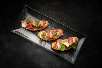 Savory Bruschetta with Salmon, Ham and Parmesan Cheese on Dark Background