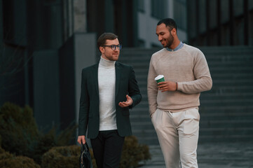 Walking and talking. Businessman in formal clothes is with black man outdoors in the city