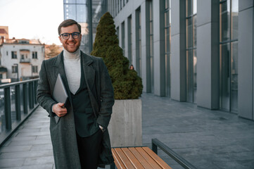 Smiling, feeling good. Handsome man in formal clothes is outdoor near the business building