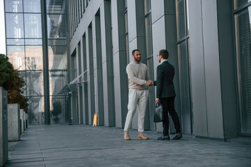 Conception of collaboration. Businessman in formal clothes is with black man outdoors in the city
