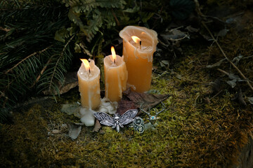 burning candles and witch amulets on moss, dark forest abstract natural background. Black magic...