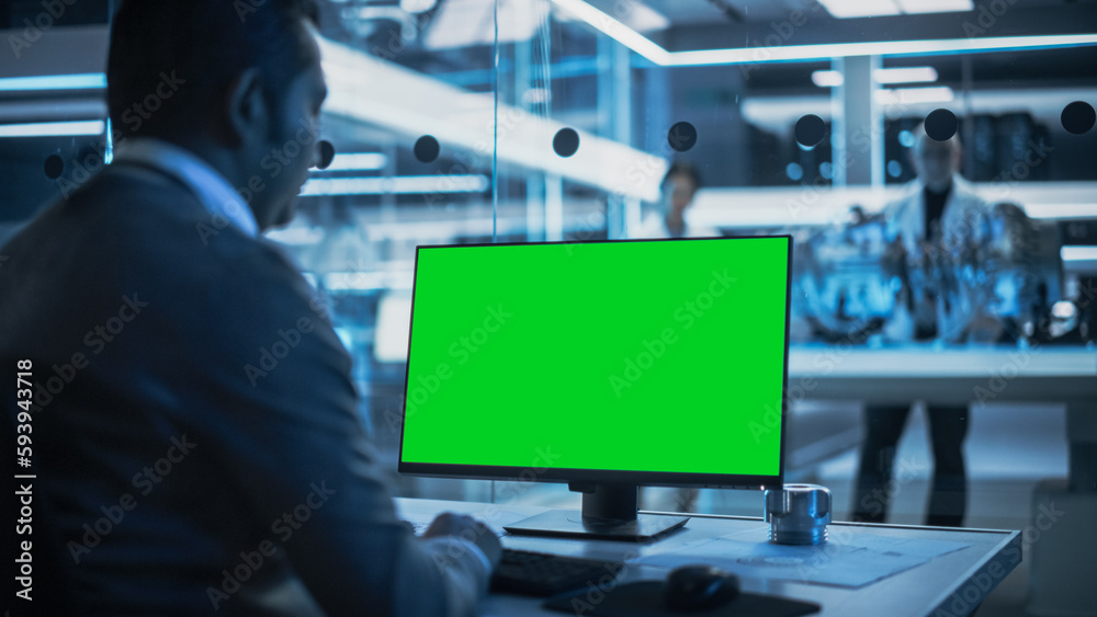 Poster Software Developer Working on Computer with Green Screen Mock Up Display. Scientific Lab, Engineering Research Center with Specialists Working on Turbine Engine Development in the Background.