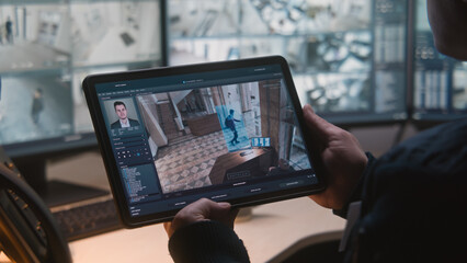Male security officer controls CCTV cameras in office, uses digital tablet and computers with surveillance camera footage playback on screens. High tech security system. Monitoring and social safety. © Framestock