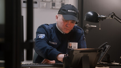 Busy security worker in headphones sits on workplace, looks view from security camera on monitor...