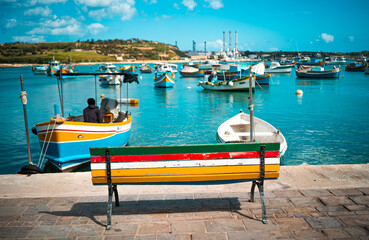 Fototapeta na wymiar A colored empty bench with a view of fisherman boats in the sea in marsaxlokk, Malta 