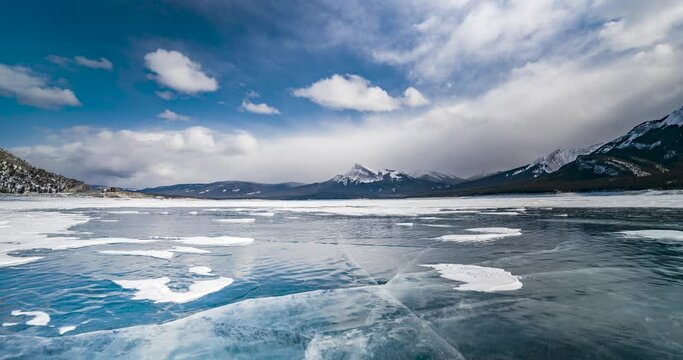 time lapse of fast moving clouds over frozen abraham lake with cracked ice and reflections on it in canadian rocky mountains