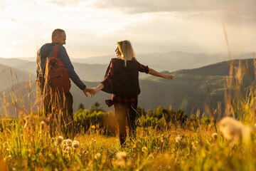 A man and a woman in tourist equipment are standing on a rock and admiring the panoramic view. A couple in love on a rock admires the beautiful views. A couple in love is traveling. A couple on a hike