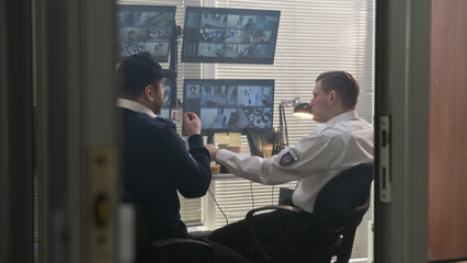 Two security guards talk, have lunch while control CCTV cameras on computers. Software showing footage of surveillance cameras with scanning system on screens. High tech security concept. Slow motion.