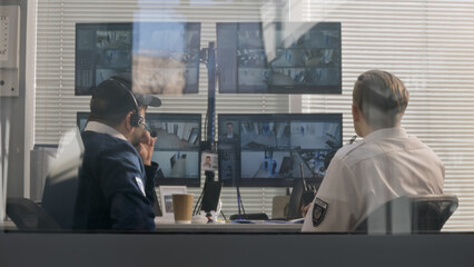 Security officers sit in surveillance room and monitor CCTV cameras with AI scanning system on computer screens using modern software. Security guard uses radio set. Concept of observation and safety.