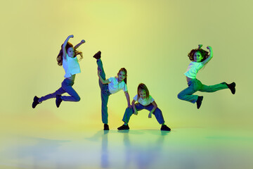Four little girls, children dancing, learning hip-hop style against green studio background in neon...