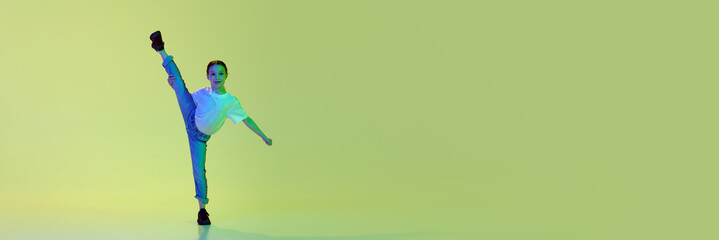 Sportive, flexible little girl, child in casual clothes dancing, training hip-hop against green studio background in neon light. Childhood, hobby, sportive lifestyle concept. Banner. Cope space for ad