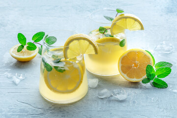 Lemonade with mint. Lemon water drink with ice. Two glasses and lemons on a pastel background. Detox beverage. Fresh homemade cocktail