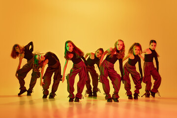 Expressive dance. Group of stylish little girls, kids, dancing, training hip-hop against yellow studio background in neon light. Concept of childhood, hobby, sportive lifestyle, education