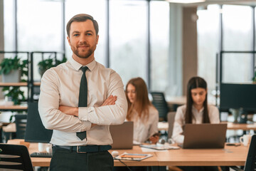 Man in tie is standing in front of his colleagues. Business people in formal clothes are working in the office together