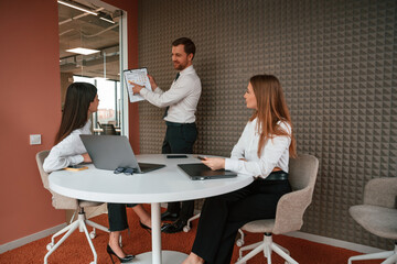 Manager is showing the plan project. Three business people are working in the office together