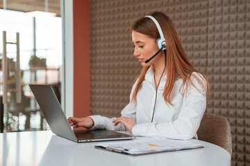 In headphones. Beautiful young woman is sitting by laptop in the office