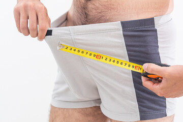 Young man holding tape measure, measuring his penis - focused at the middle of tape measure. - obrazy, fototapety, plakaty
