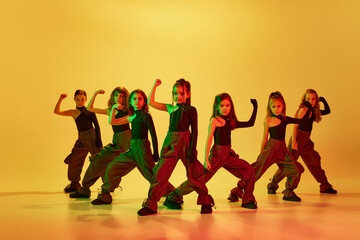 Group of talented kids, autistic children in stylish clothes dancing, performing hip-hop against yellow studio background in neon light. Concept of childhood, hobby, sportive lifestyle