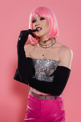 Portrait of stylish drag queen in gloves biting finger on pink background.