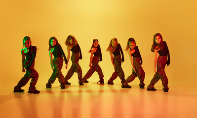 Little artistic girls, children in sport style clothes dancing hip-hop against yellow studio...