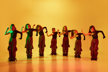 Group of talented kids, autistic children in stylish clothes dancing, performing hip-hop against yellow studio background in neon light. Concept of childhood, hobby, sportive lifestyle