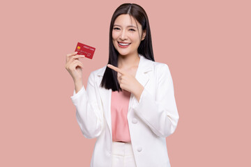 Beautiful young Asian business woman wearing white suit smiling, showing, presenting credit card for online payment isolated on pink background.