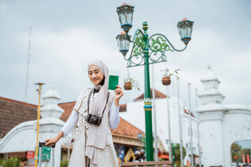 female traveller with hijab smiling and bring the passport while standing at the sidewalk