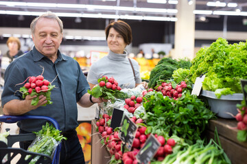 elderly man chooses radish in vegetable and fruit department