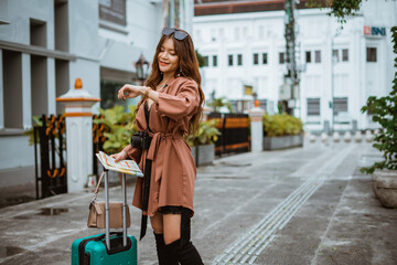 female traveller looking at her watch while standing at the sidewalk bring her travel equipment