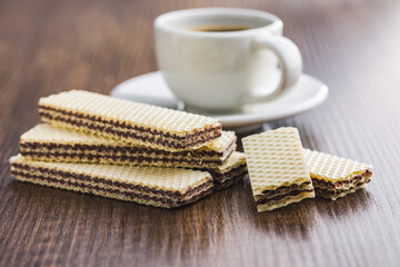 Sweet chocolate wafer and coffee cup on wooden table.