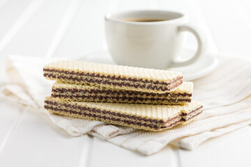 Sweet chocolate wafer and coffee cup on white table.
