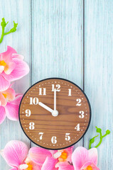 An Alarm clock and pink streaked orchid flower on blue wooden background.