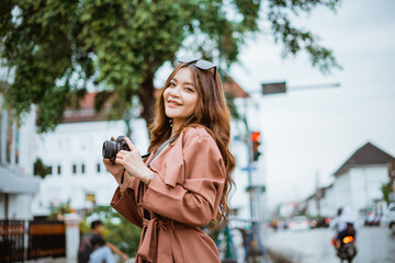 female traveller with long brown hair smiling while standing at the sidewalk and holding the camera