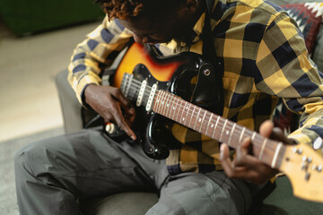 Obraz premium Young joyful african american man playing guitar in living room. Happy man enjoy at home..