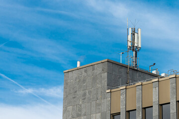 Broadcasting antenna on the roof of the big administrative building. Blue sky with light white...