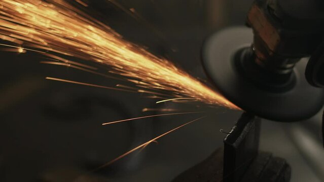 Sparks fly in slow motion as angle grinder grinds away steel edge in vice clamp on workbench