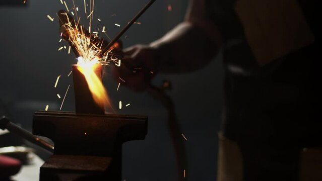 Red hot metal throws sparks as it is welded in a vice on a bench in a metalworkers workshop