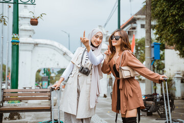 two female travellers bring their trunks and pointing with their finger while standing at the sidewalk