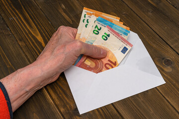 A man's hand puts European money banknotes into a white envelope lying on the table. Close up.