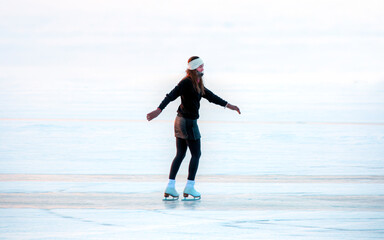 A young happy woman is skating on the transparent ice of the frozen Lake Baikal on a sunny winter...