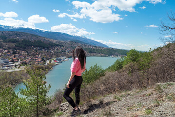 Naklejka na ściany i meble Traveler woman standing high above a blue lake with stunning panoramic view .Traveling in the nature in Bulgaria 
