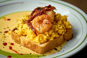 Toast with scrambled eggs, shrimp and hollandaise sauce in a plate on a wooden background