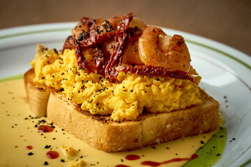 Toast with scrambled eggs, shrimp and hollandaise sauce in a plate on a wooden background