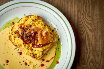 Toast with scrambled eggs, shrimp and hollandaise sauce in a plate on a wooden background