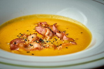 Pumpkin cream soup with bacon in a plate on a wooden background