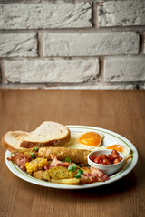 English breakfast with sausages, scrambled eggs, beans and toast in a plate on a wooden background